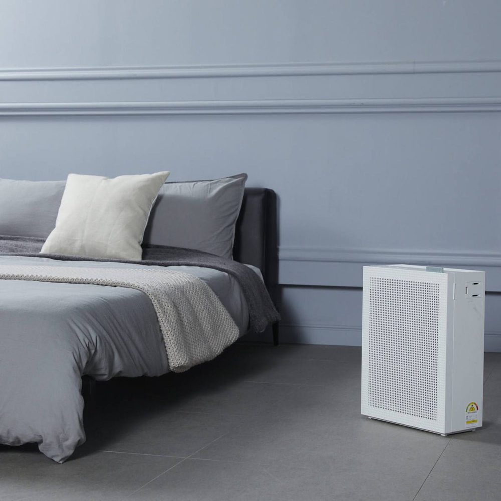 Coway Airmega 150 på gulvet ved siden af en seng