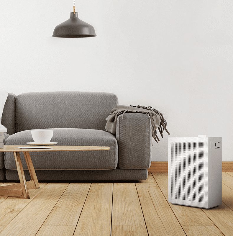 Coway Airmega 150 i hvid på et trægulv ved siden af en grå sofa