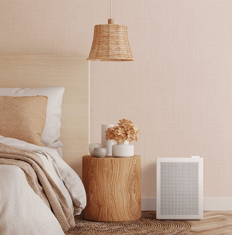 Coway Airmega 150 i hvid ved siden af et sidebord i et soveværelse